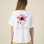 Femme de dos portant un t-shirt blanc à manches courtes avec une illustration de fleur d'hibiscus rouge et bleue et l'inscription "Botanical Study No.23".