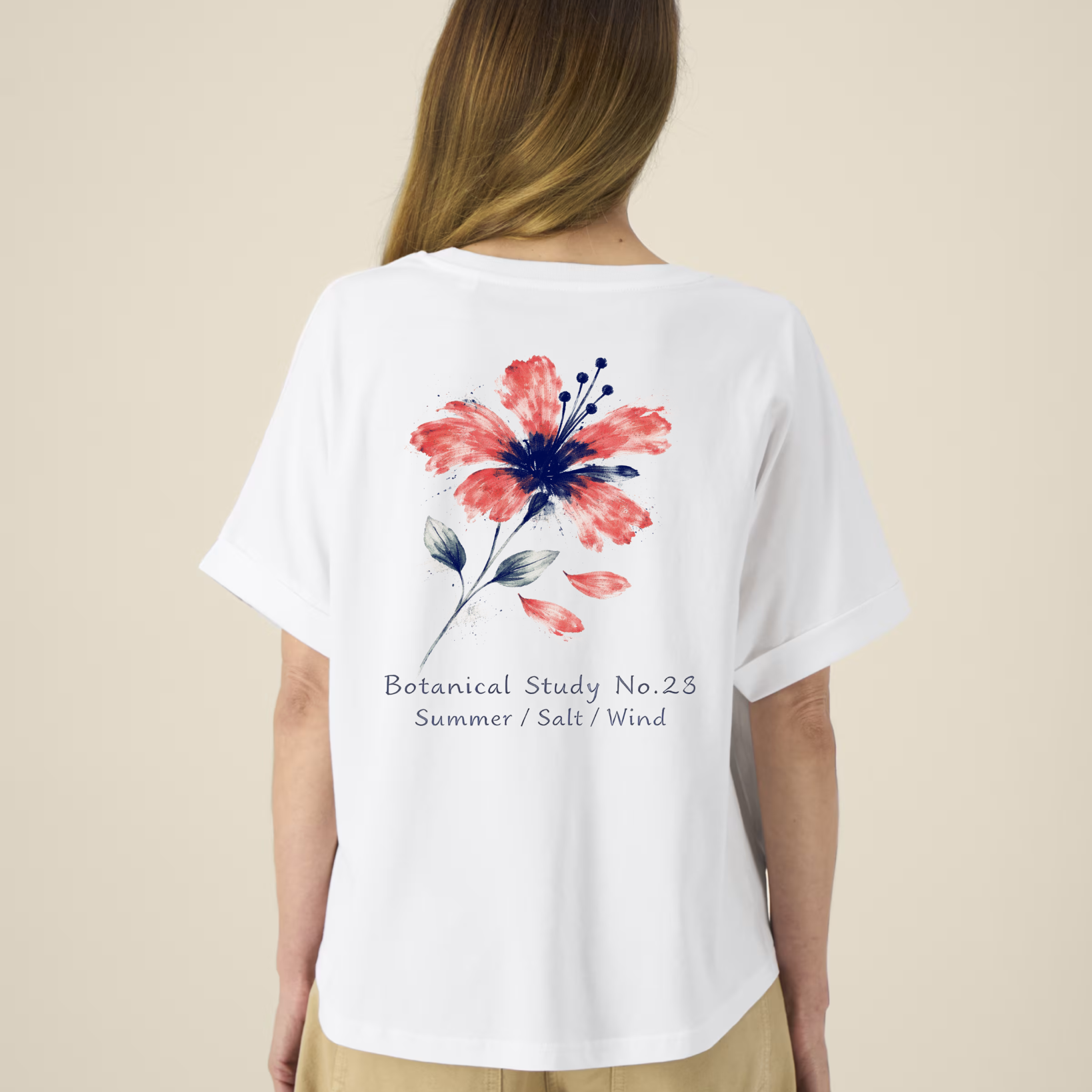 Femme de dos portant un t-shirt blanc à manches courtes avec une illustration de fleur d'hibiscus rouge et bleue et l'inscription "Botanical Study No.23".
