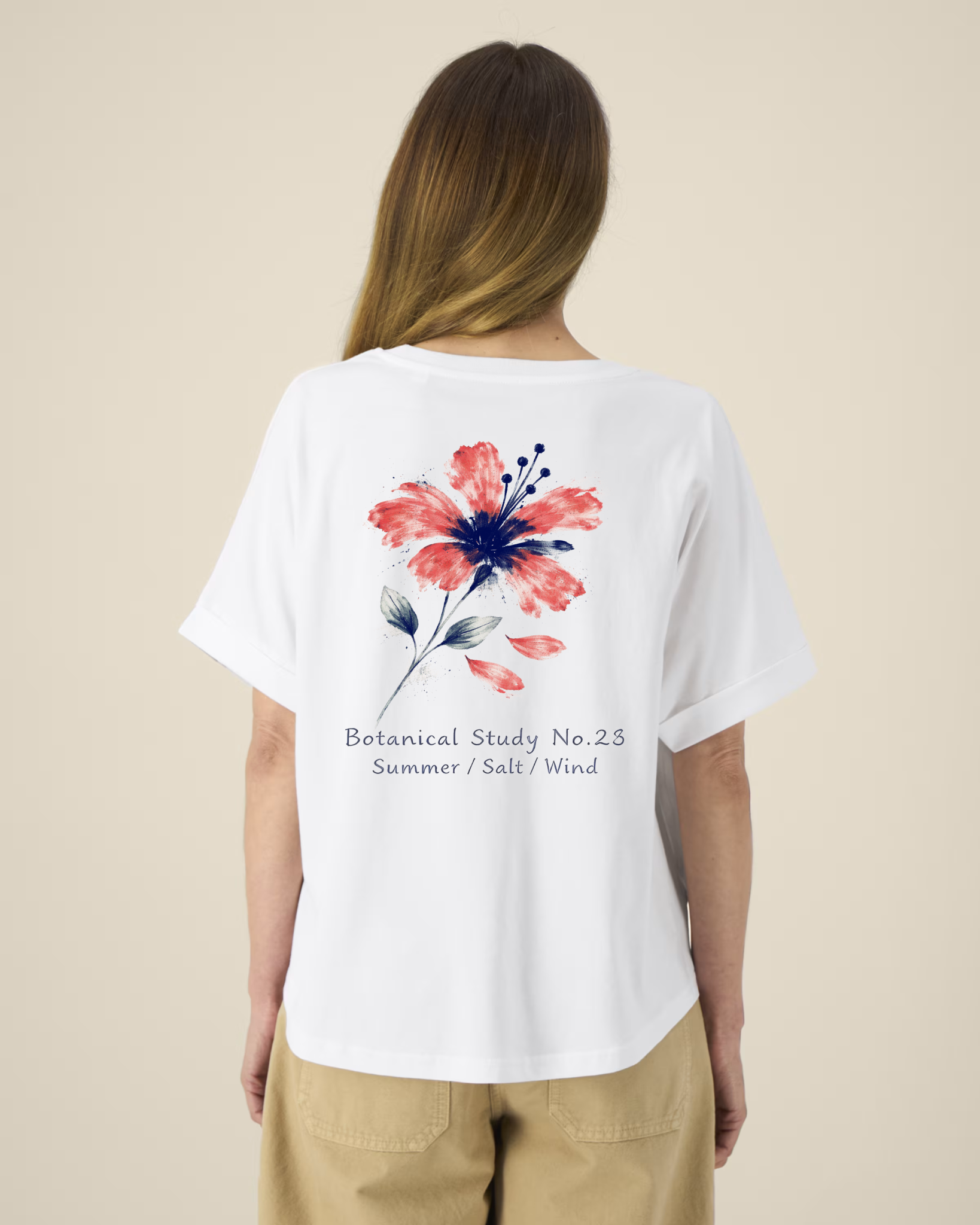 Femme de dos portant un t-shirt blanc à manches courtes avec une illustration de fleur d'hibiscus rouge et bleue et l'inscription "Botanical Study No.23".