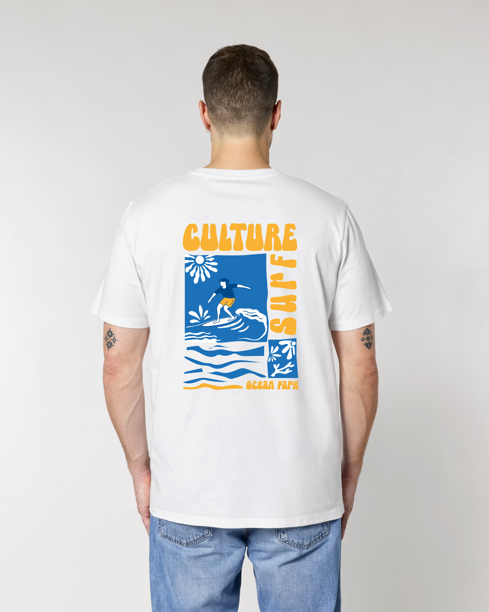 Vue de dos d'un homme portant un t-shirt blanc Ocean Park, affichant un grand graphisme carré avec un surfeur sur une vague, un soleil stylisé et l'inscription "CULTURE SURF" en lettres jaunes.
