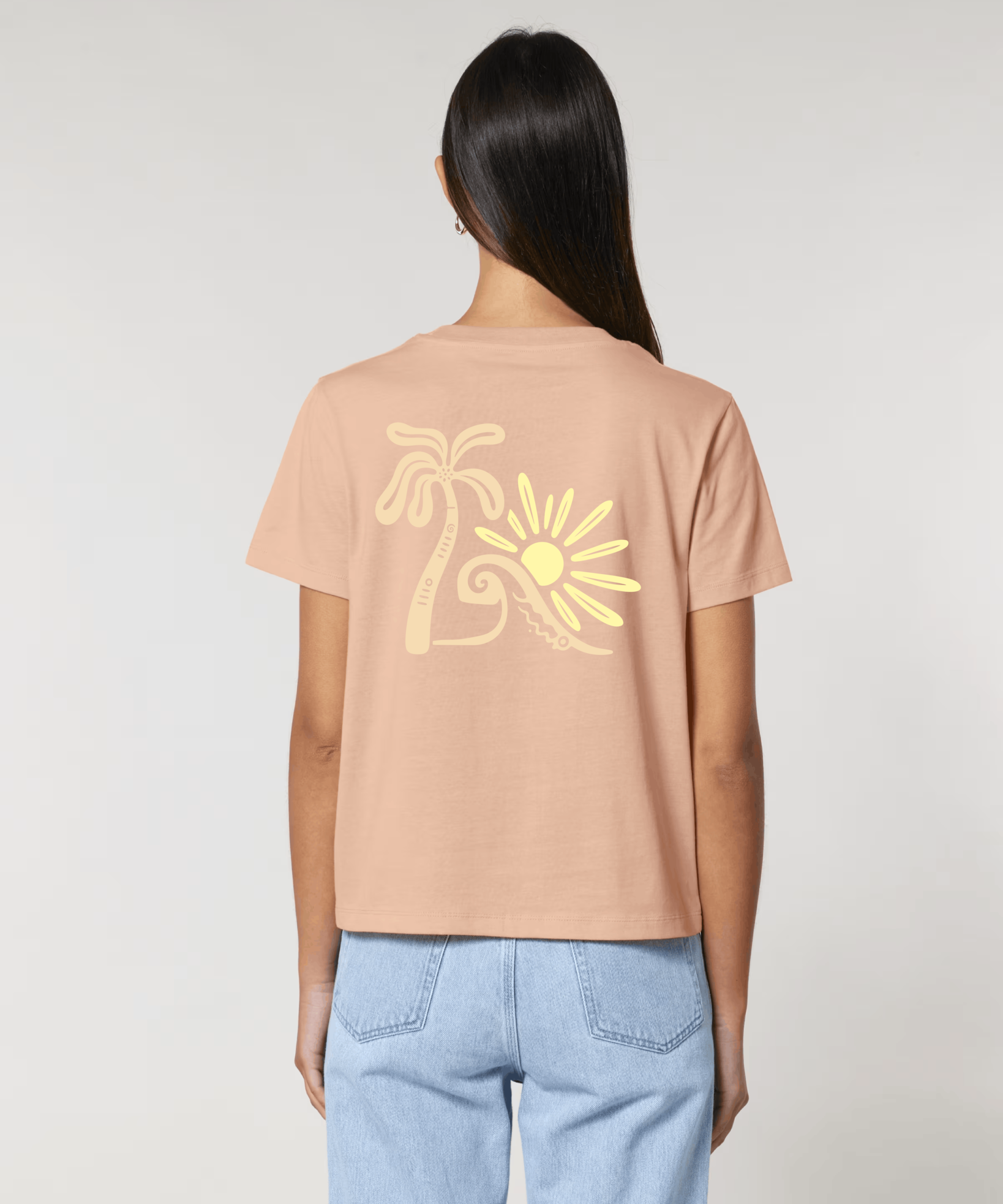 Vue de dos d'une femme portant un t-shirt couleur pêche avec une grande illustration jaune pâle représentant un palmier, une vague et un soleil stylisés.