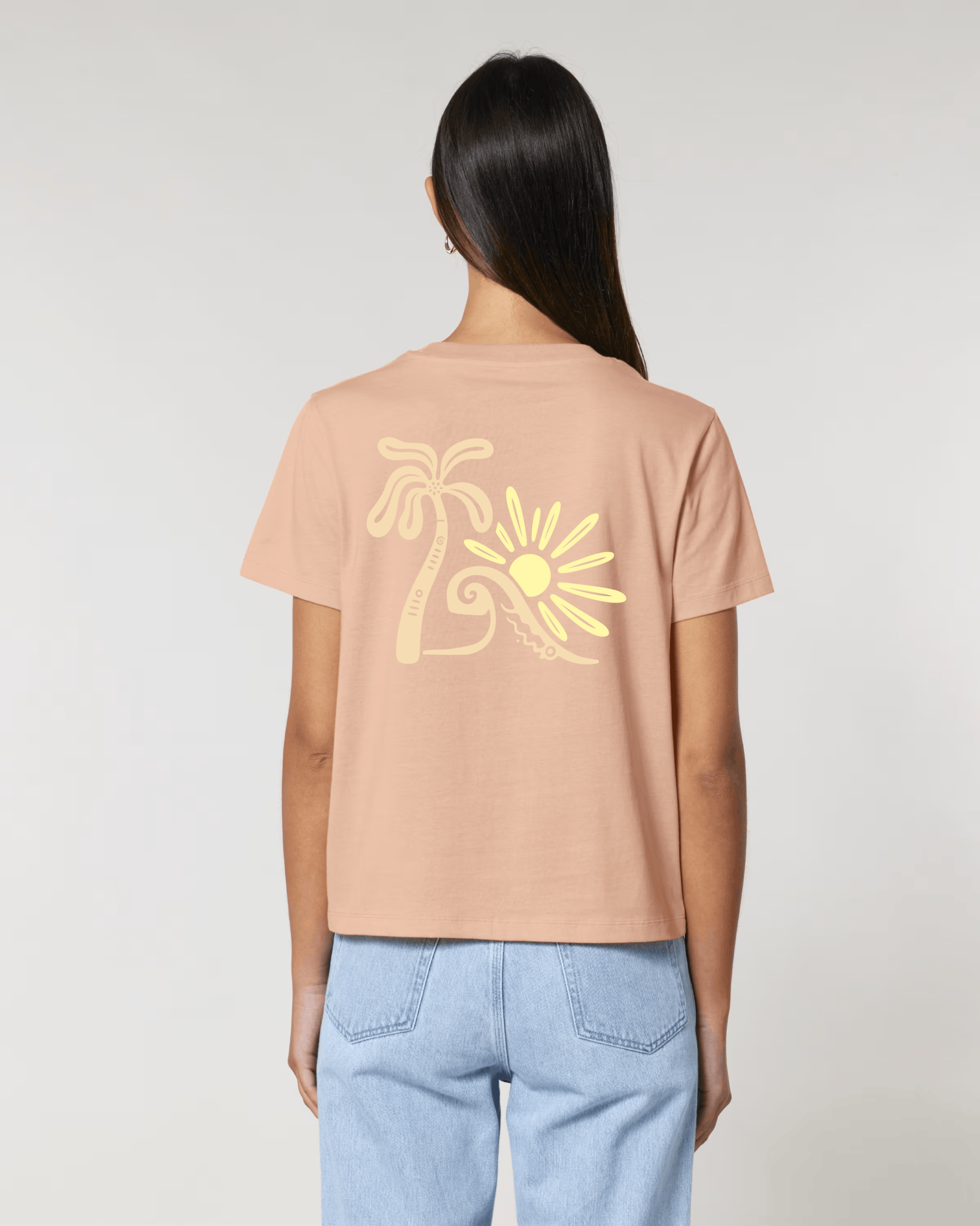 Vue de dos d'une femme portant un t-shirt couleur pêche avec une grande illustration jaune pâle représentant un palmier, une vague et un soleil stylisés.