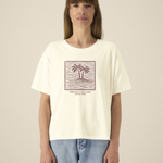 Femme de face portant un t-shirt de couleur crème avec une illustration centrale bordeaux représentant deux palmiers sur une île entourée de vagues dans un cadre carré, avec l'inscription "PROTECT NATURE OCEAN PARK".