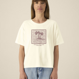 Femme de face portant un t-shirt de couleur crème avec une illustration centrale bordeaux représentant deux palmiers sur une île entourée de vagues dans un cadre carré, avec l'inscription "PROTECT NATURE OCEAN PARK".