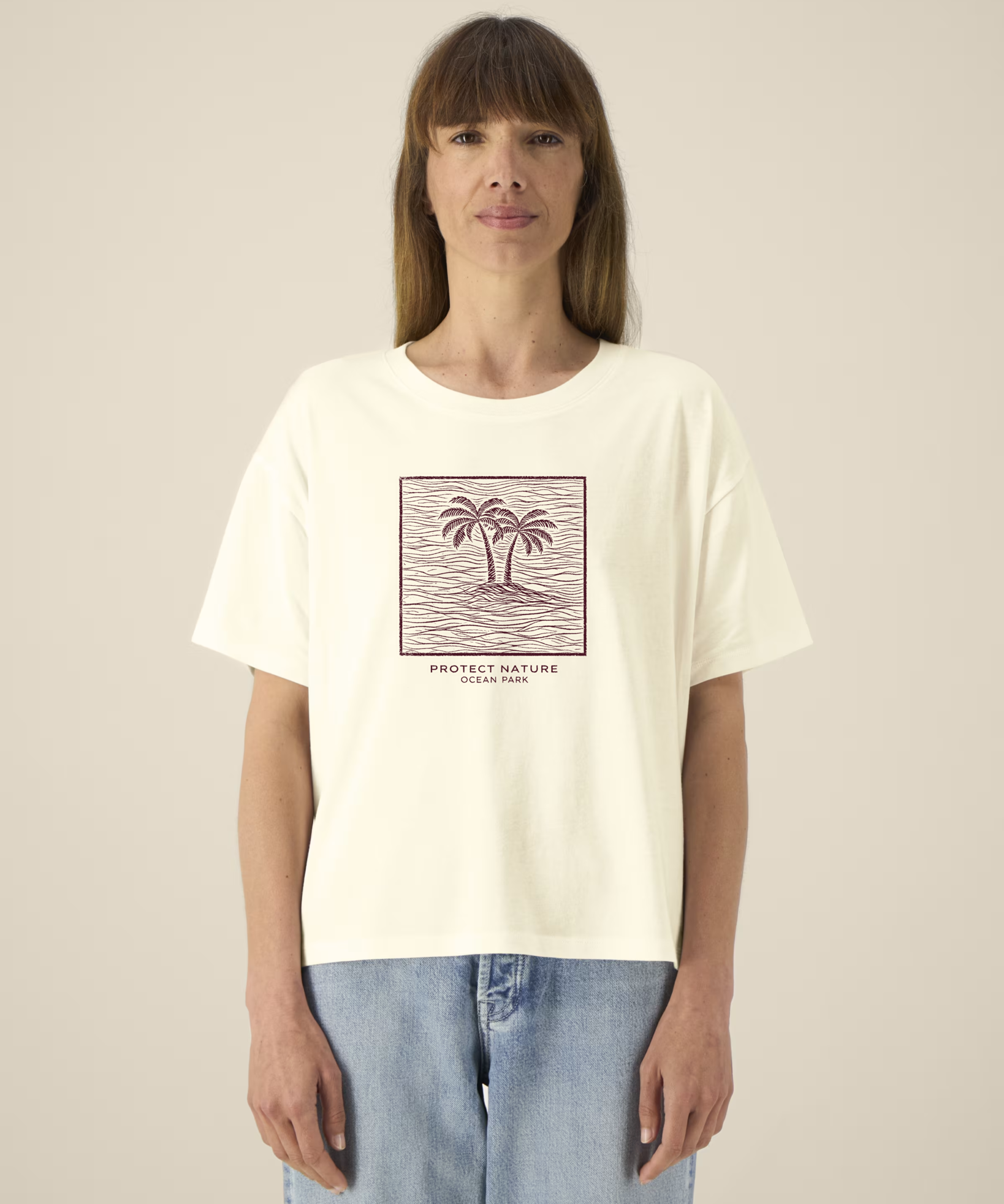 Femme de face portant un t-shirt de couleur crème avec une illustration centrale bordeaux représentant deux palmiers sur une île entourée de vagues dans un cadre carré, avec l'inscription "PROTECT NATURE OCEAN PARK".