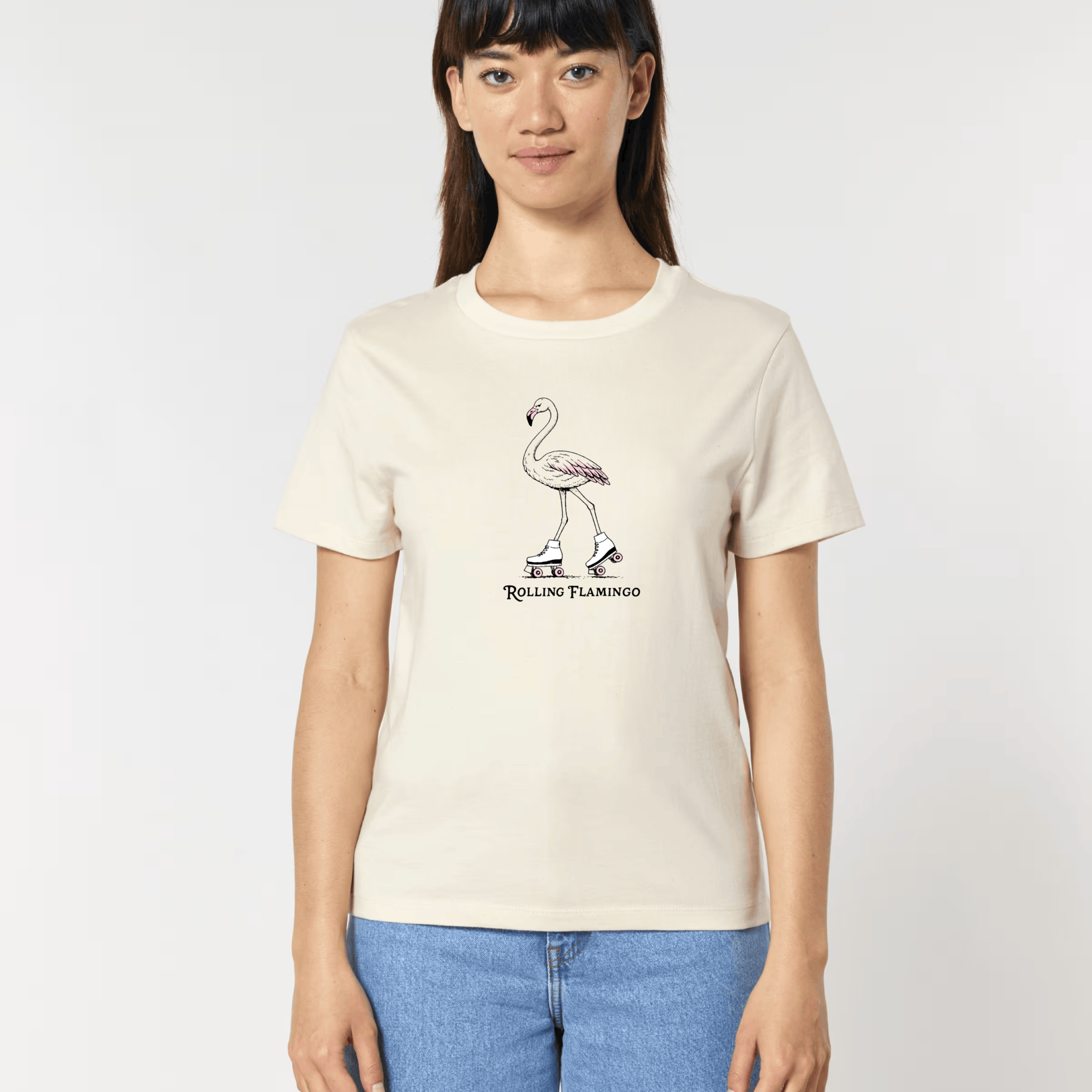 Femme de face portant un t-shirt blanc cassé avec une illustration centrale d'un flamant rose chaussé de patins à roulettes rétro, surmontant l'inscription "Rolling Flamingo".