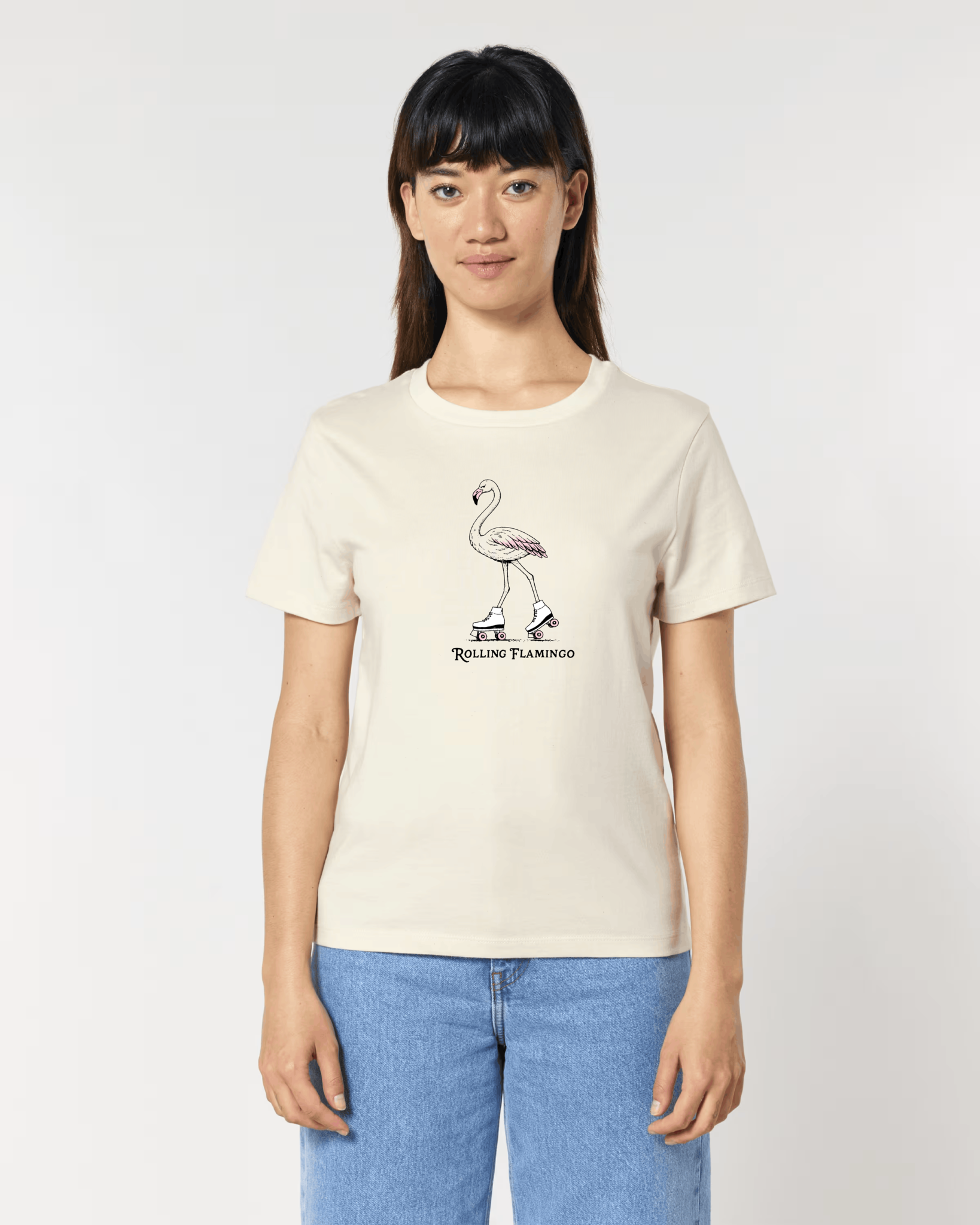 Femme de face portant un t-shirt blanc cassé avec une illustration centrale d'un flamant rose chaussé de patins à roulettes rétro, surmontant l'inscription "Rolling Flamingo".