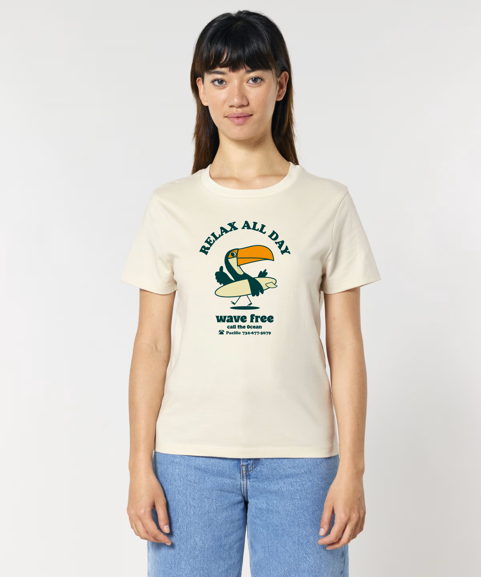 Femme de face portant un t-shirt de couleur blanc cassé naturel avec une illustration centrale d'un toucan tenant une planche de surf, entouré des textes "RELAX ALL DAY" et "wave free call the Ocean".