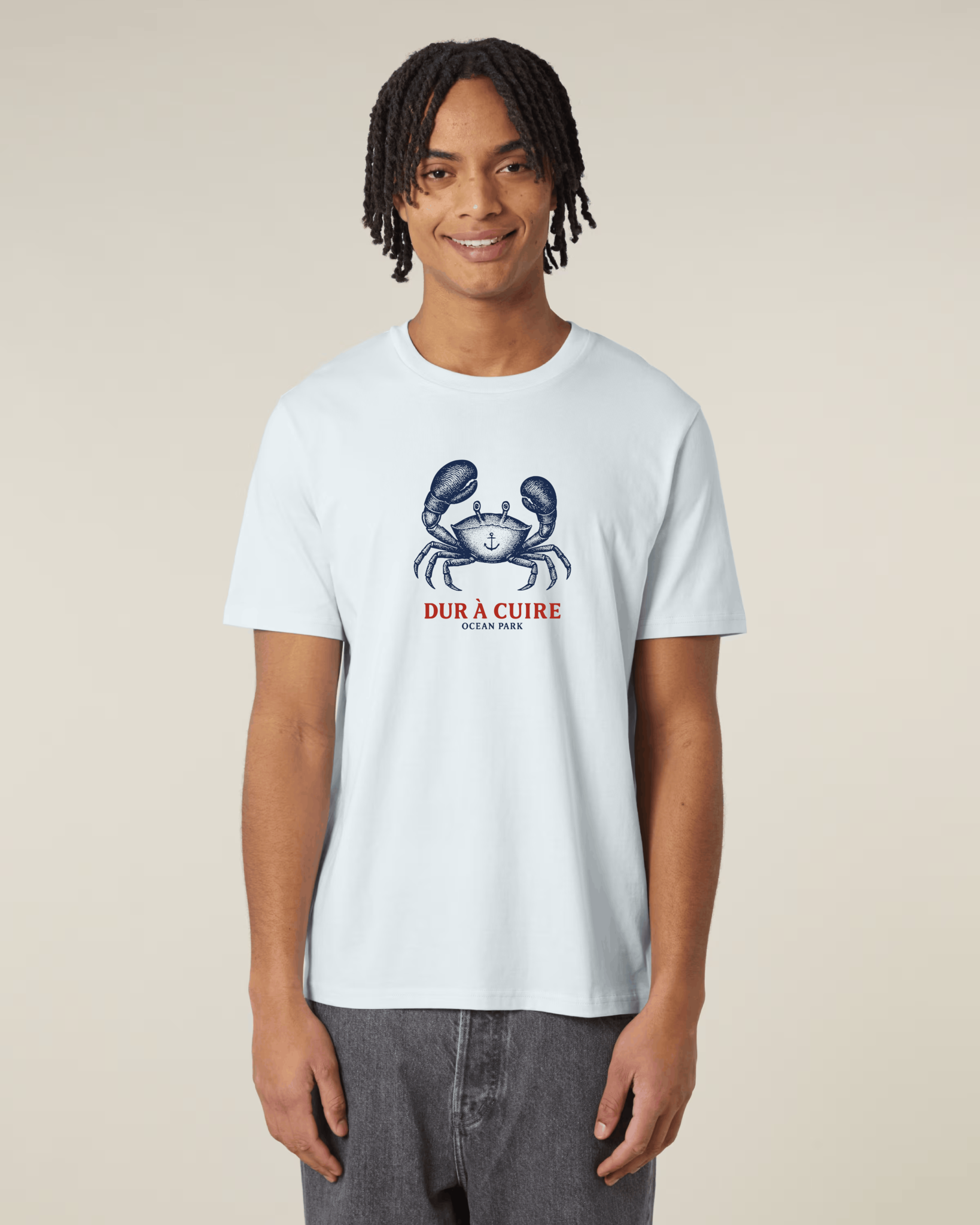 Homme de face portant un t-shirt bleu azur très clair avec une illustration centrale d'un crabe bleu marine arborant un tatouage d'ancre sur sa carapace.
Le texte rouge "DUR À CUIRE" est inscrit juste au-dessous du dessin avec la mention "OCEAN PARK" en plus petit.