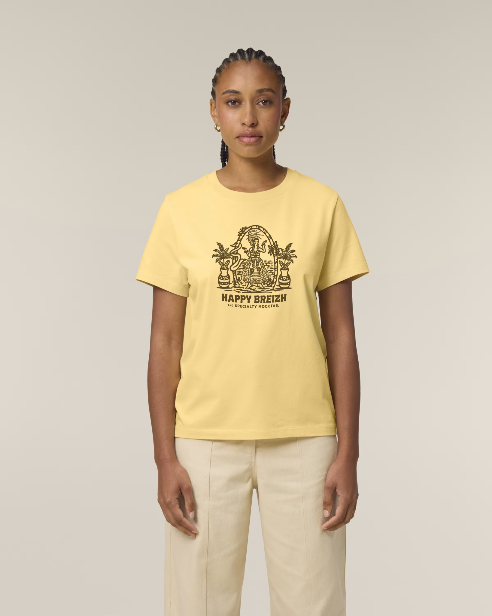 Femme de face portant un t-shirt jaune clair avec une illustration marron représentant une bigoudène dans un décor de plage tropicale avec palmiers et l'inscription "HAPPY BREIZH".