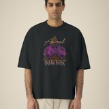 Homme portant un t-shirt noir oversize avec un graphisme central composé d'un triangle au motif léopard, de deux têtes de léopards violets de profil et des inscriptions "Animal" et "OCEAN PARK" en style néon rétro.