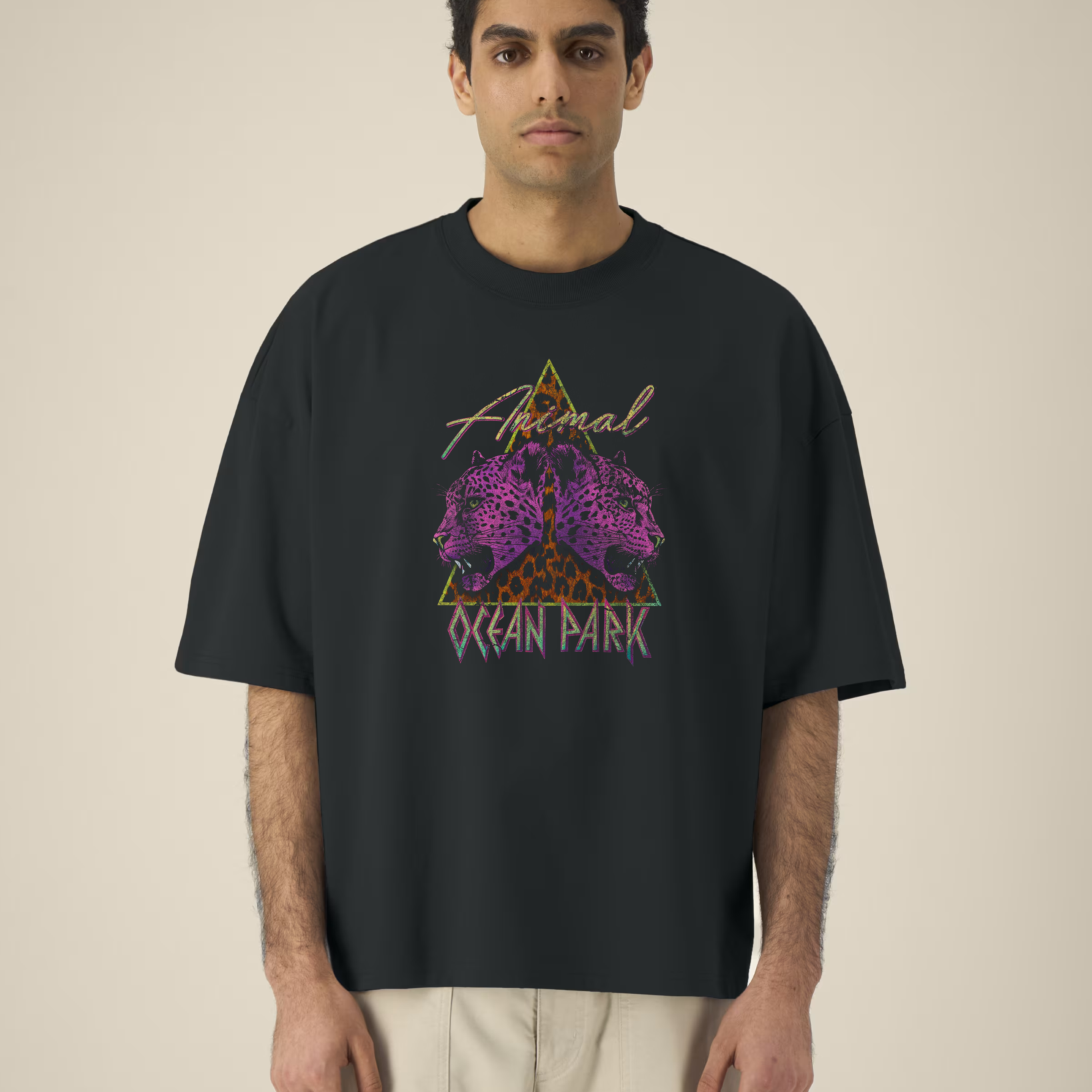Homme portant un t-shirt noir oversize avec un graphisme central composé d'un triangle au motif léopard, de deux têtes de léopards violets de profil et des inscriptions "Animal" et "OCEAN PARK" en style néon rétro.