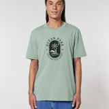 Homme de face portant un t-shirt de couleur vert aloe avec un graphisme central en forme de badge noir contenant un palmier, une planche de surf, une vague et un croissant de lune, entouré du texte "Ocean Park - Explore The Coast".