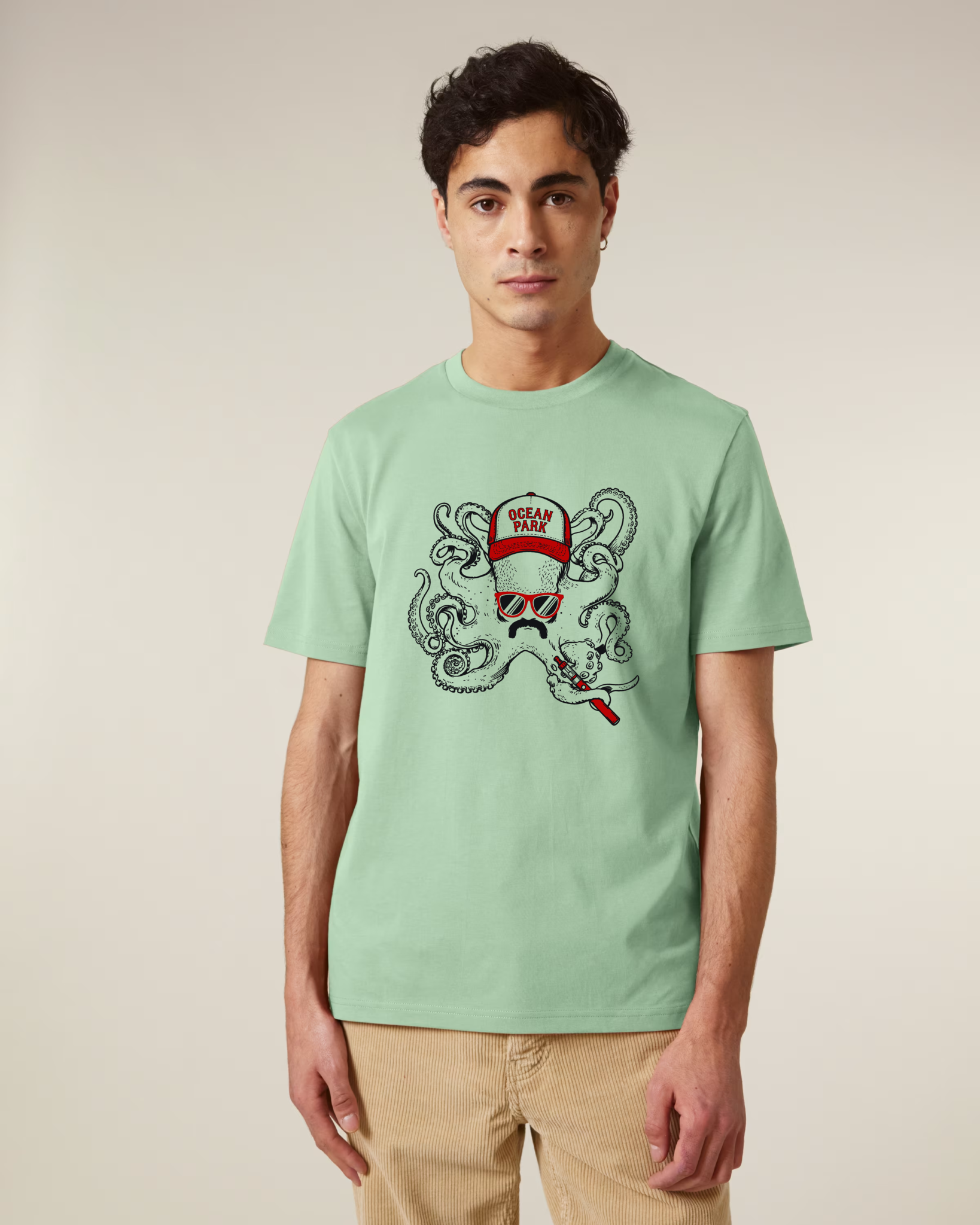Homme de face portant un t-shirt vert misty jade avec une illustration centrale d'un poulpe portant une casquette rouge Ocean Park, des lunettes de soleil rouges, une moustache, et tenant une cigarette électronique.