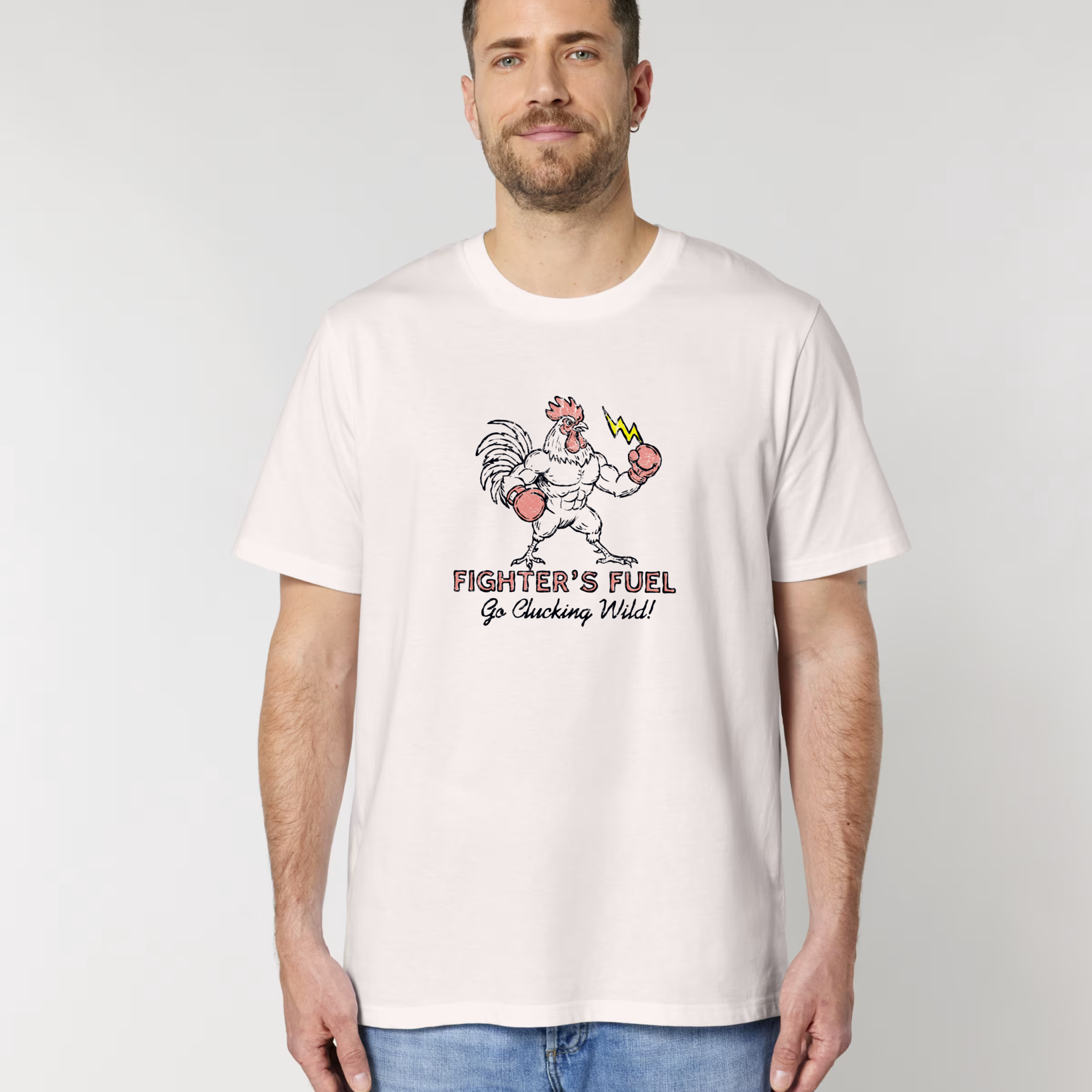 Homme de face portant un t-shirt blanc vintage avec une illustration centrale d'un coq musclé en gants de boxe tenant un éclair, sous le texte "FIGHTER'S FUEL - Go Clucking Wild!".
