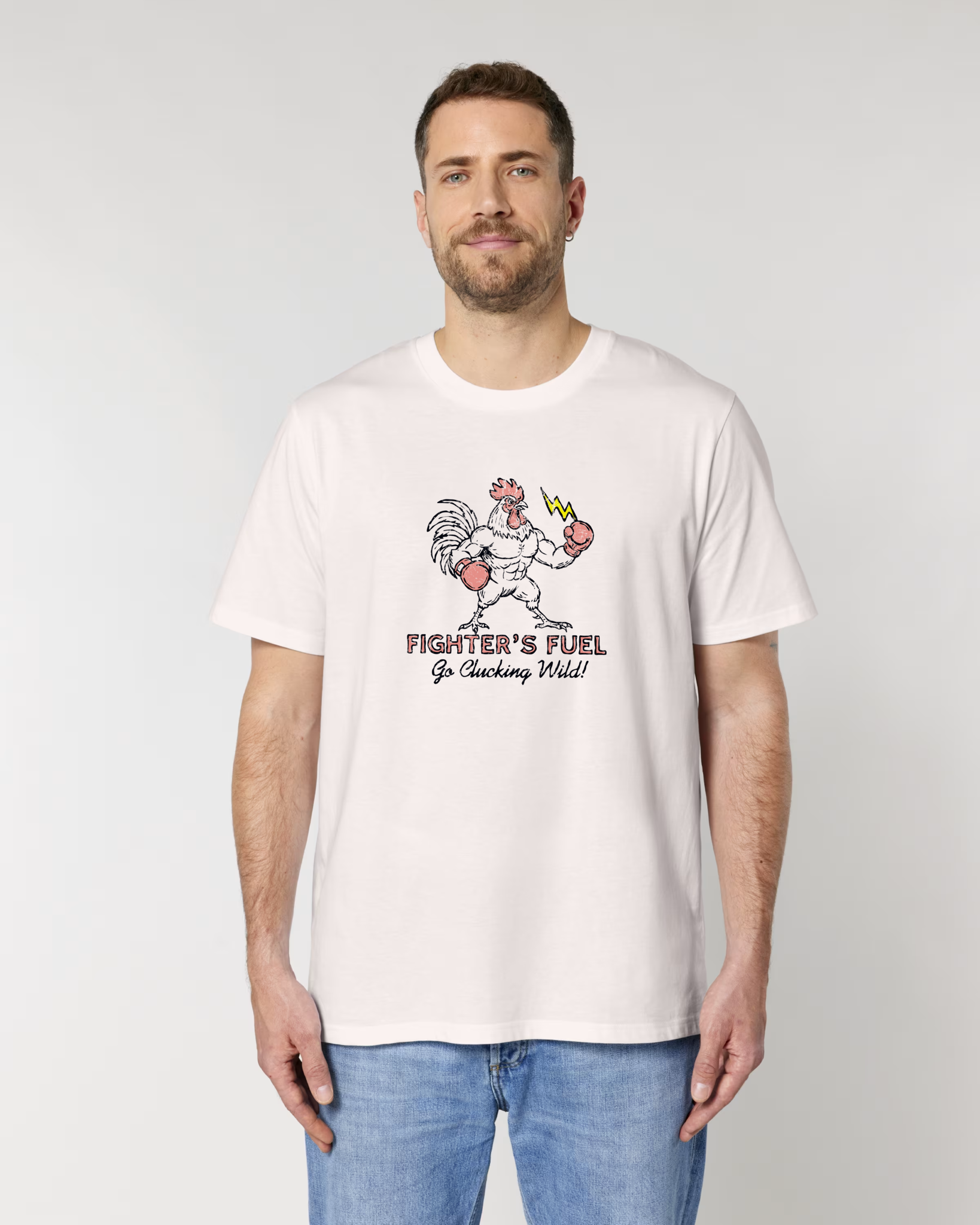 Homme de face portant un t-shirt blanc vintage avec une illustration centrale d'un coq musclé en gants de boxe tenant un éclair, sous le texte "FIGHTER'S FUEL - Go Clucking Wild!".