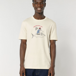 Un homme souriant portant un t-shirt de couleur crème (écru) avec une illustration d'un marin en marinière chevauchant un gros thon comme un cowboy, avec l'inscription rouge "BREIZH COW-BOY".