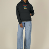 Sweat à capuche oversize noir Ocean Park Halloween, petit print squelette et grimoire sur le devant, porté avec un jean large