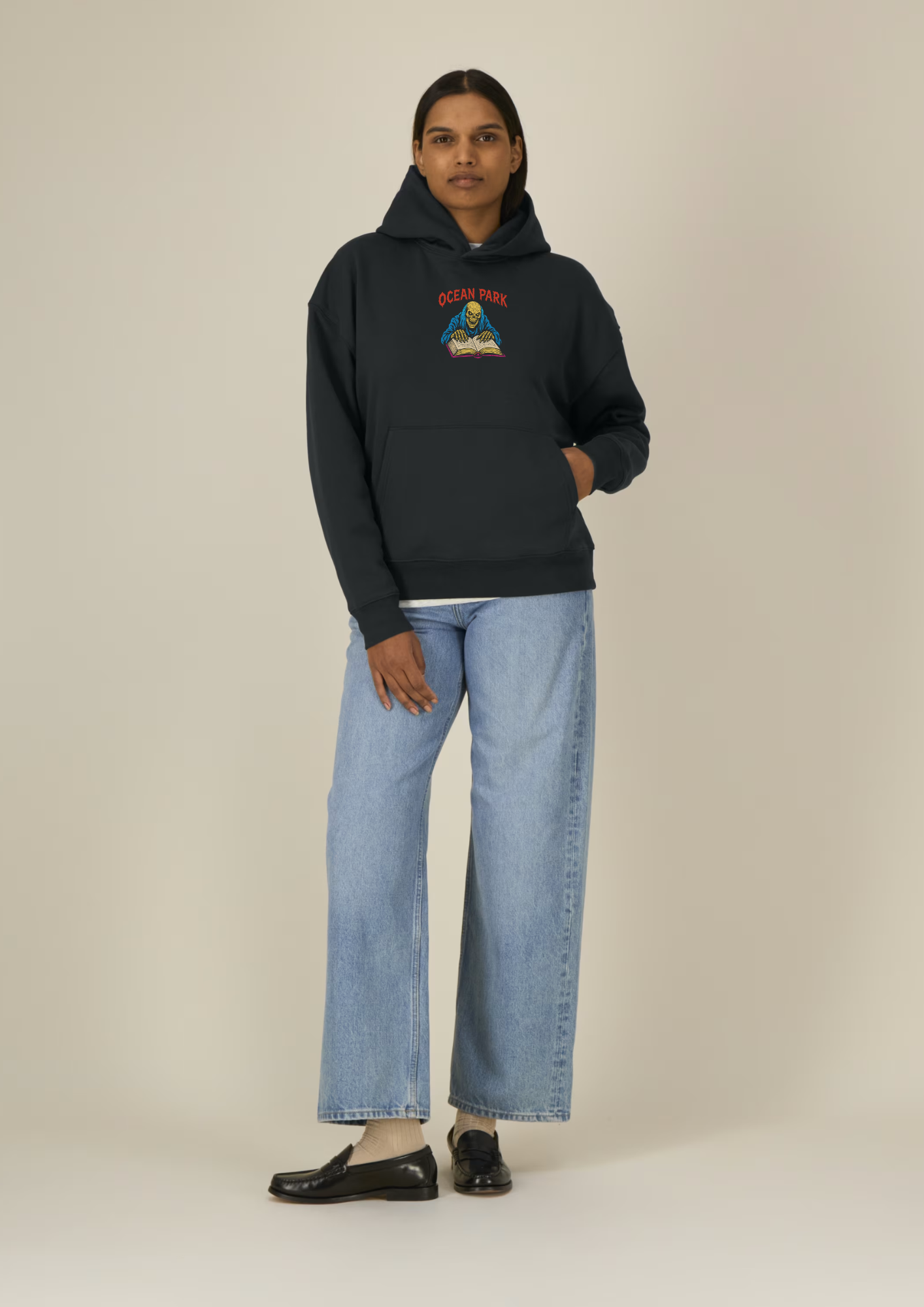 Sweat à capuche oversize noir Ocean Park Halloween, petit print squelette et grimoire sur le devant, porté avec un jean large